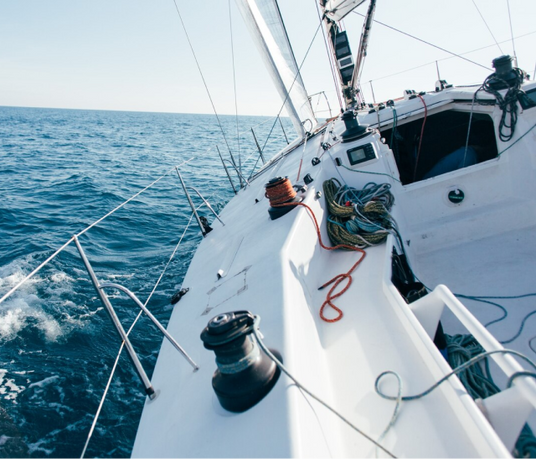 Close-up view of a sailing yacht cutting through the ocean waves with ropes and rigging on deck.